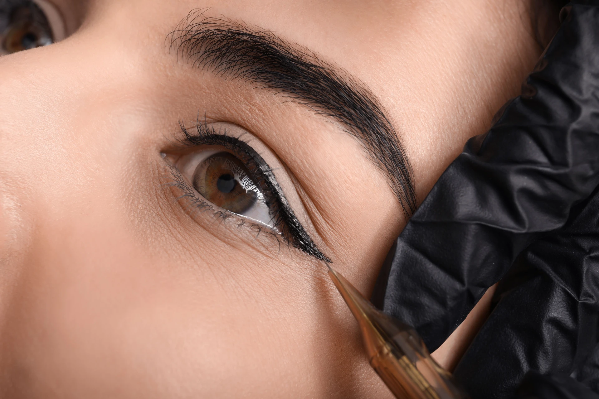 Winged eyeliner tattoo procedure in progress—artist carefully creating a sharp, lifted wing along the upper lash line in Rockland County NY. 