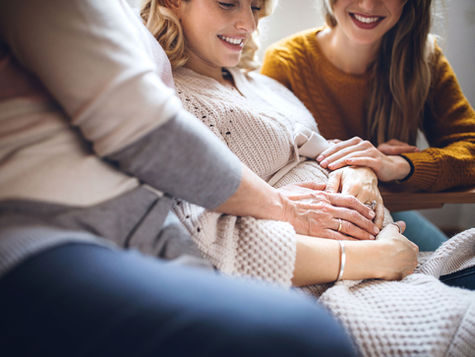 A surrogate women with a pregnant belly and multiple women touching her belly.