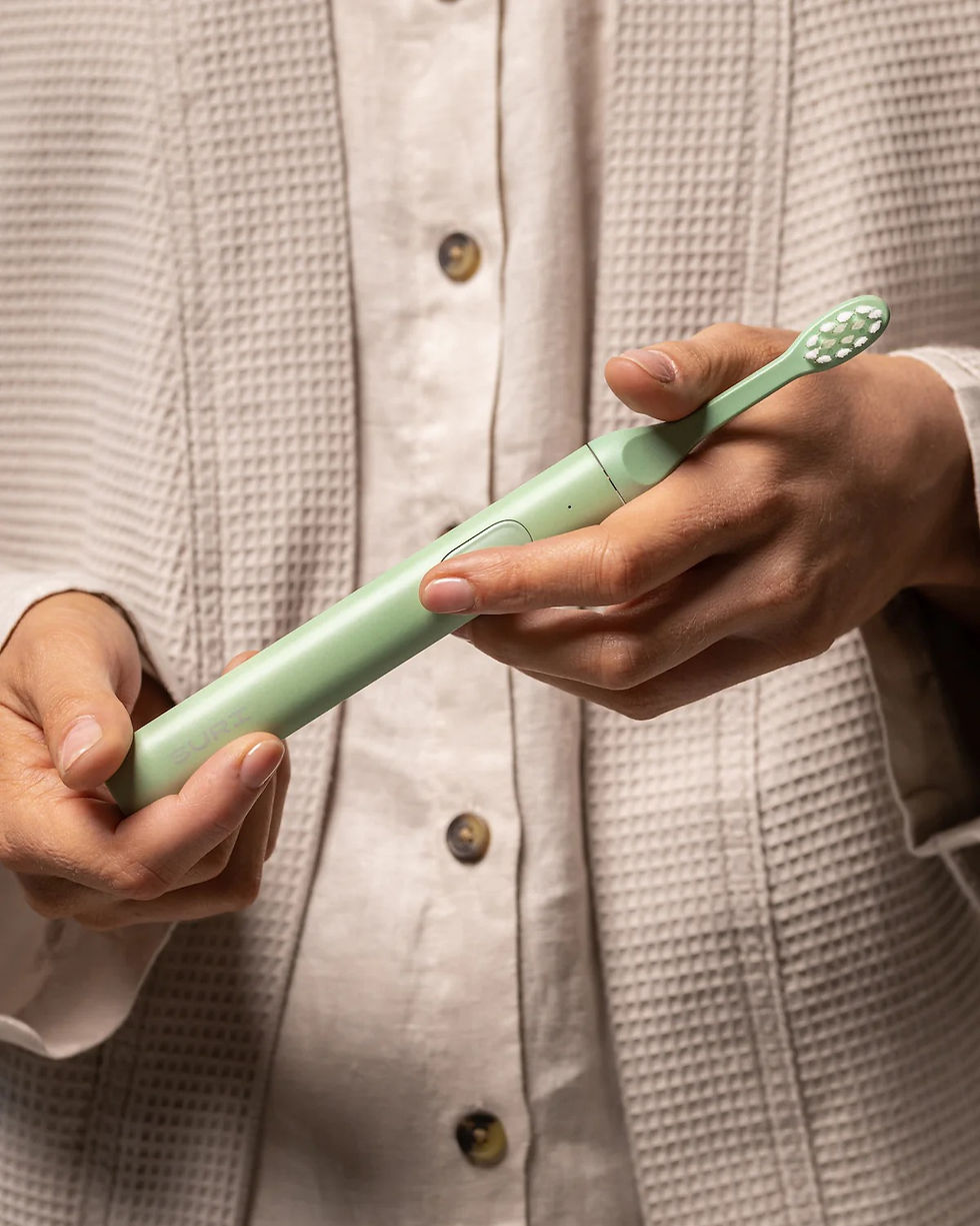 a person holding a green suri sustainable electric toothbrush in their hands