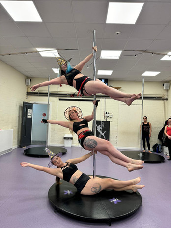 Three women performing pole fitness poses together