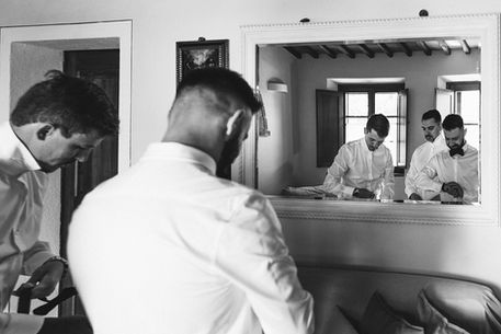 and white portrait of reflex in the mirror of best men and groom getting ready for wedding in Tuscany
