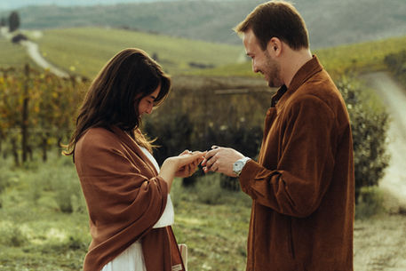 boyfriend putting on engagement ring in girlfriend's hand in a scenic vineyard in Tuscany