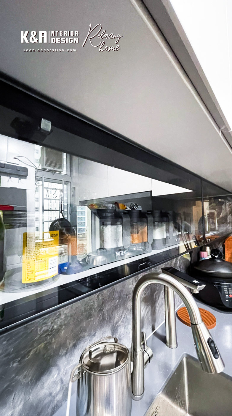 【廚房設計】經典L形廚房設計之下，以中灰調大理石紋理石材與暖白、深灰高質板材建構，盡顯高貴氣派，尺寸精準的訂造廚櫃組合，為戶主提供便利的入廚體驗，其中工作枱上強化玻璃吊櫃以「上翻門」設計，更便利於日常