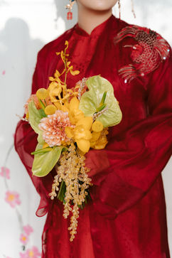 Bride in a red qipao holding a yellow floral bouquet – garden wedding at home, Vietnam