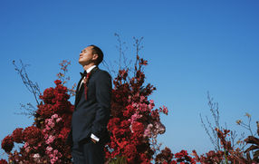 Groom in navy tuxedo standing before red floral display – Hoiana Resort