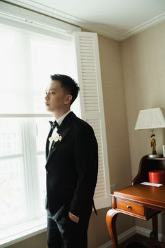 Groom in a black tuxedo looking out a window at Park Hyatt – Park Hyatt Saigon