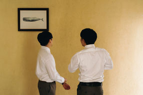Groom and groomsman in white shirts against yellow wall – Thailand