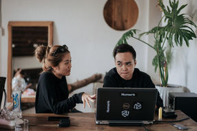 A woman and man discuss work behind a Numark laptop – Da Lat