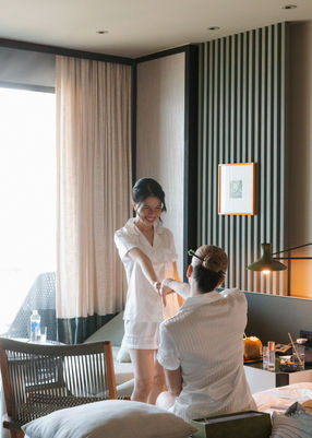 Bride in white pajamas laughing with friend in hotel room – Hoiana Resort