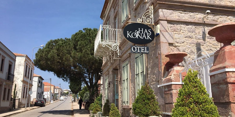 Taş bina üzerinde "Has Konak Otel" tabelası, sokakta ağaçlar ve diğer binalar. Güneşli bir gün, sakin ve eski bir mahalle.