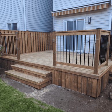 Wooden deck with black metal railings, steps, and a privacy fence in a backyard. Bushes to the left and an air conditioning unit right.