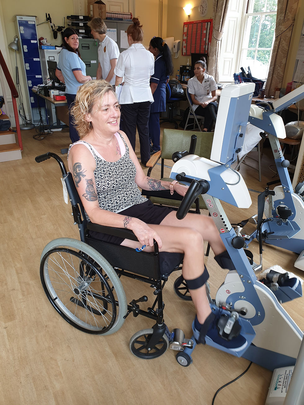 Linda, smiling in her wheelchair, operates accessible exercise bike/pedal equipment.
