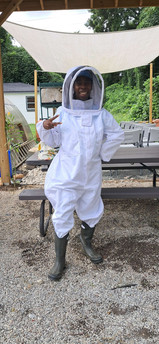 Lady wearing a white bee suit holding a up the peace sign with her fingers