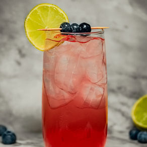 Shirley Temple-mocktail i høyt glass med is, bær på pinne og limeskive