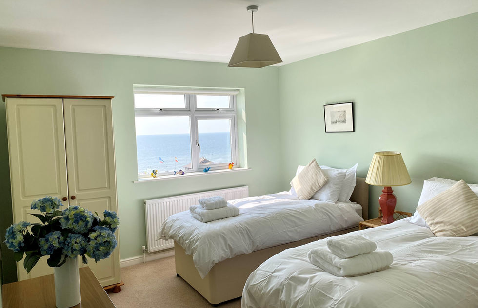 A bedroom with two single beds in with white sheets and white towels at the end of the bed and you can see the sea from the window.