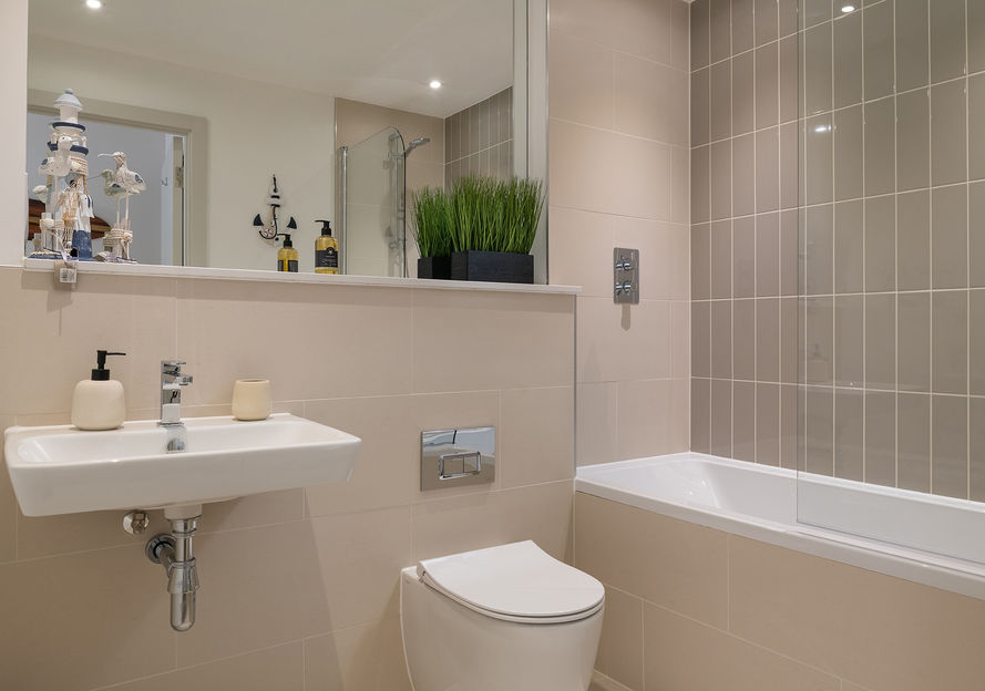 A modern bathroom with a white sink, white toilet and a built in bath with a large mirror.