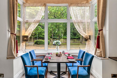 Dining table with blue chairs by a large window.
