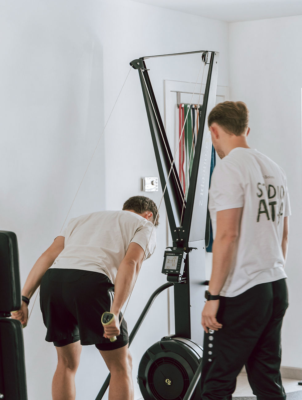 Persoon traint op een ski-ergometer onder begeleiding van een coach van Studio ACTif in een moderne trainingsruimte."