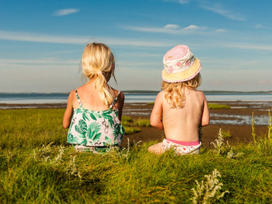 Zwei Kinder sitzen am Wattenmeer und beobachten die Gezeiten