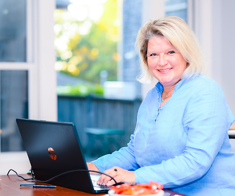 Brand Strategist Kris Kiehn smiles at the camera while sitting at a table with an open laptop computer