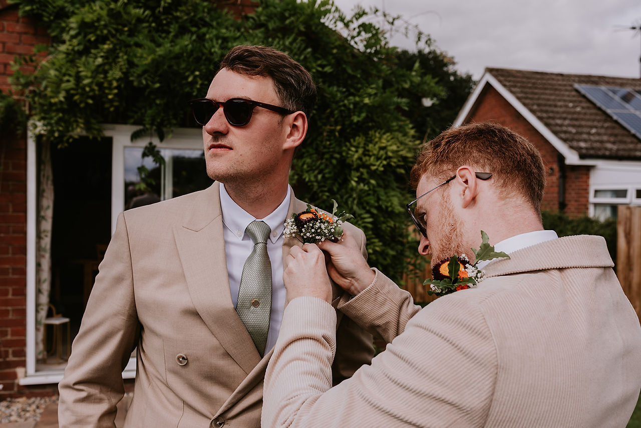 Groom Mike is wearing sunglasses and getting his buttonhole put on ready for the wedding
