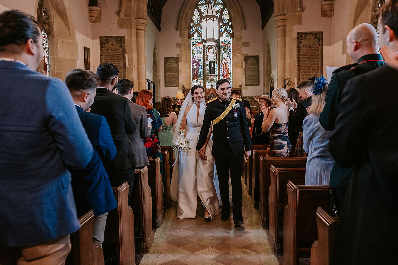 The bride and groom walk hand in hand back up the aisle after their wedding ceremony. They are smiling at their guests while they all applaud their exit.