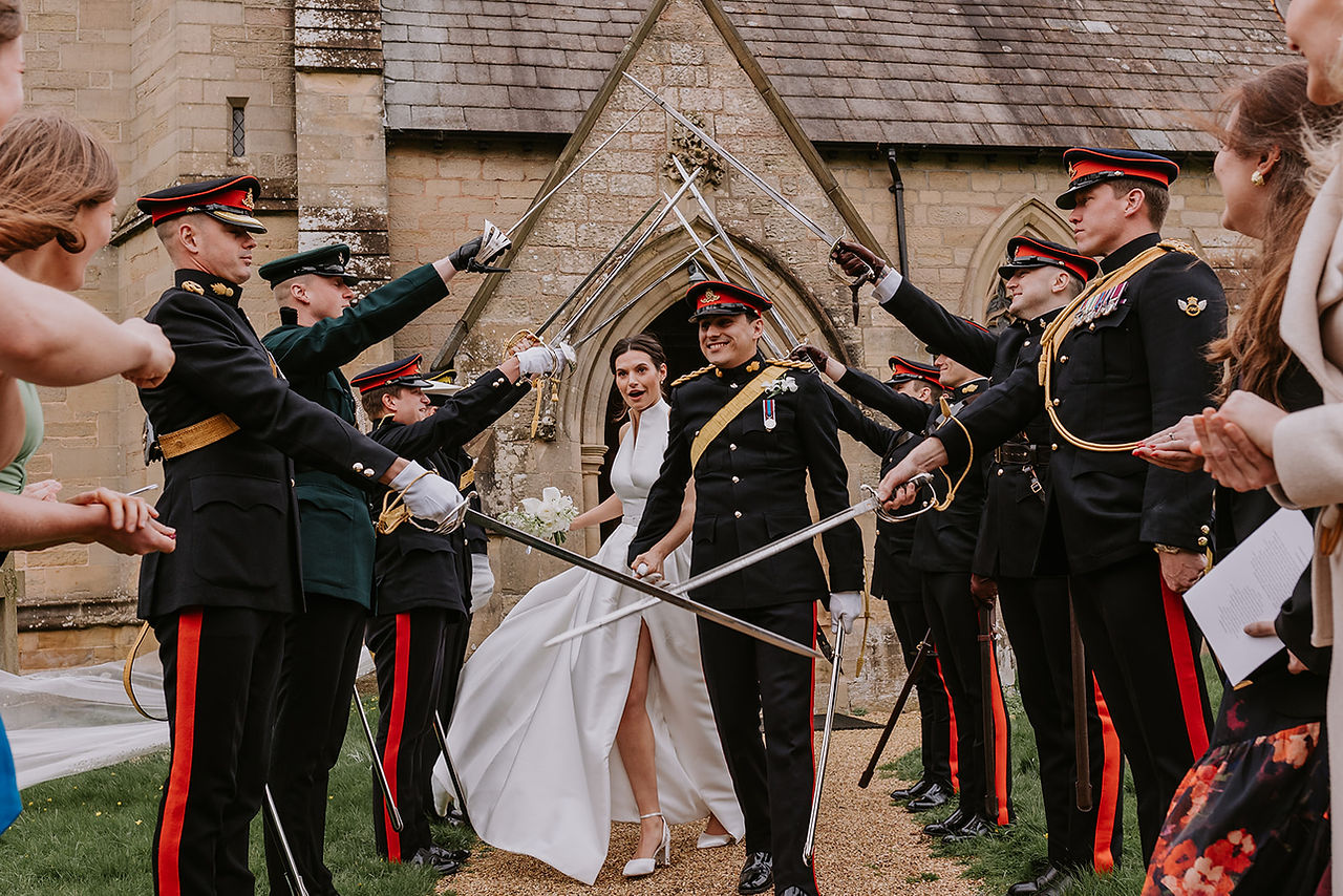 The brides veil flies away during their walk through the guard of honour outside of the church near Lodge Farm Weddings.