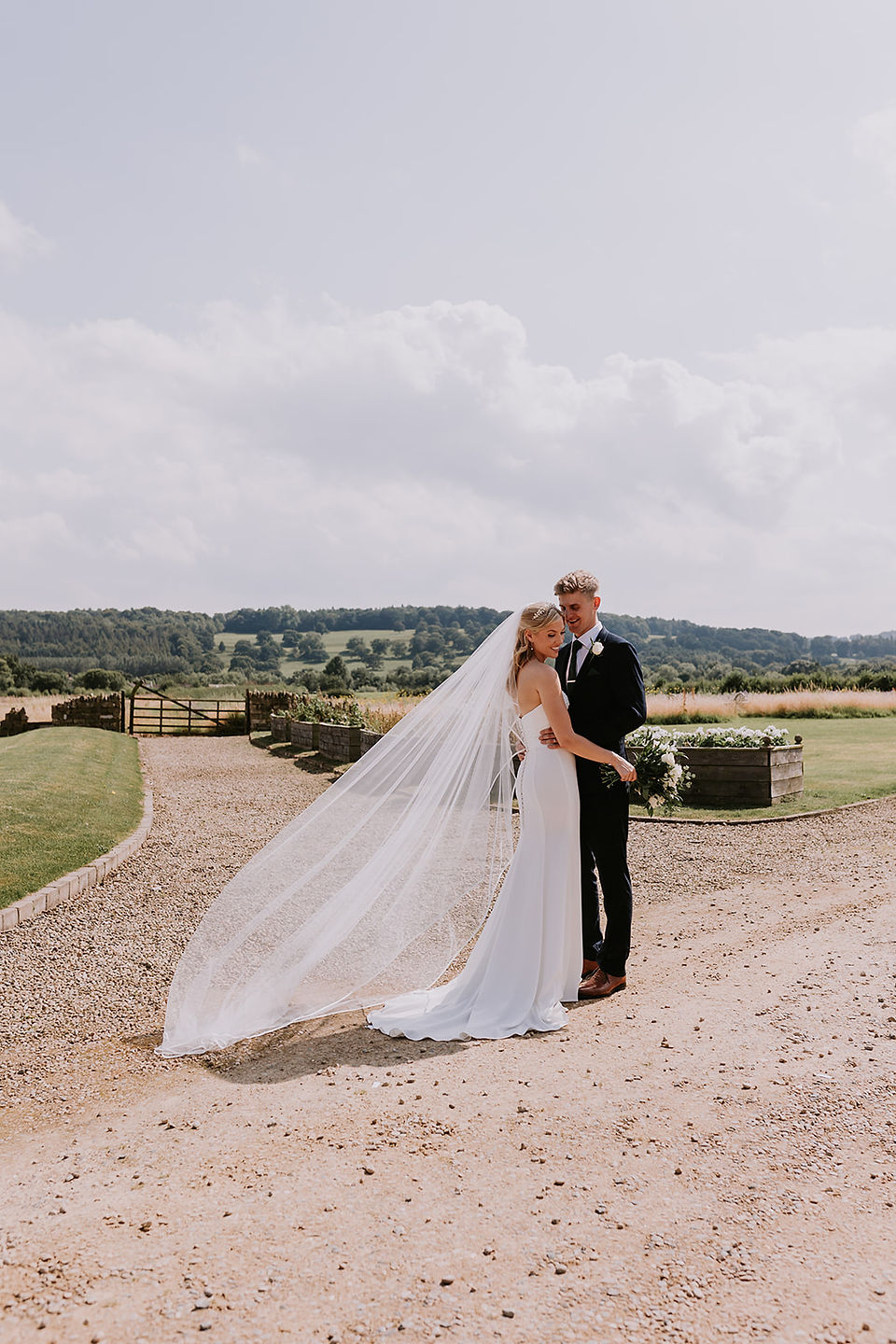 The bride and groom are looking at each other lovingly in the grounds at Wharfedale Grange. The groom is holding the bride at the waist and her veil is floating in the wind. 