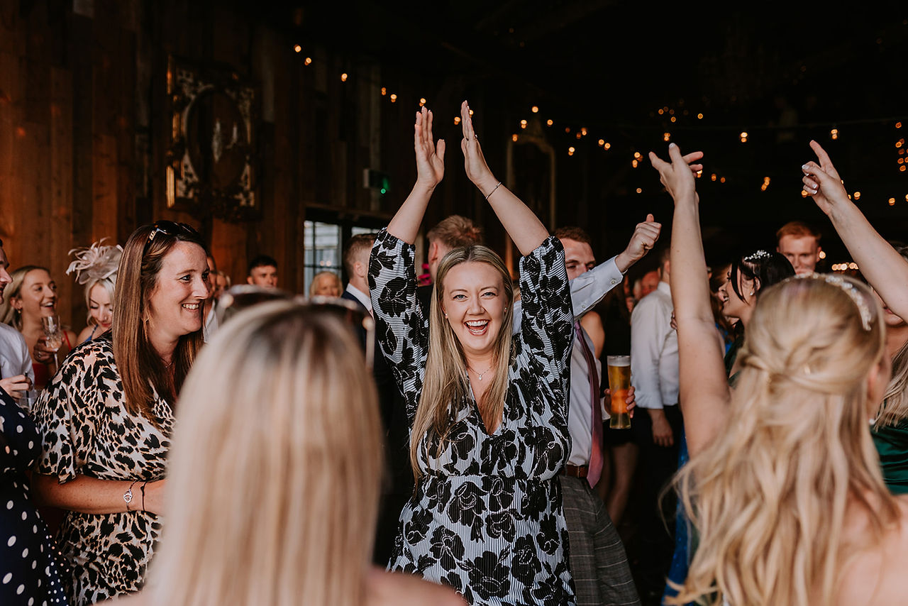 A wedding guest is dancing and throwing her arms in the air on the dance floor at Wharfedale Grange.