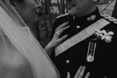 The brides hand is gently touching the grooms military uniform  so that her wedding ring is visible.