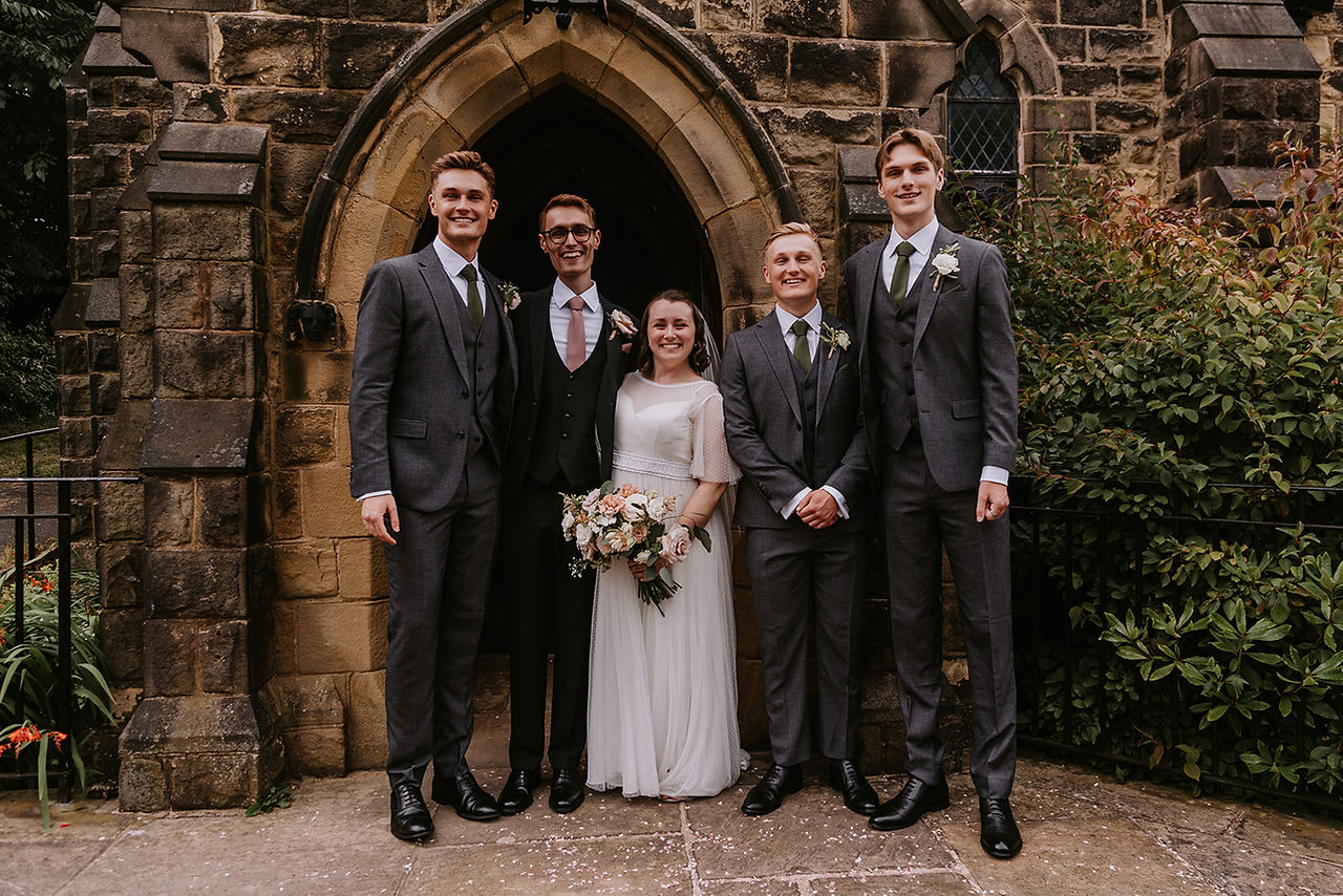 The bride and groom pose for a moment with the groomsmen outside of the church.