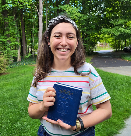 Netta Asner holding a blue book outdoors in front of trees. Netta Asner | Jewish Educator