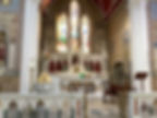 The interior of the church at Saul, the altar lit beneath tall stained glass windows and a carved reredos.