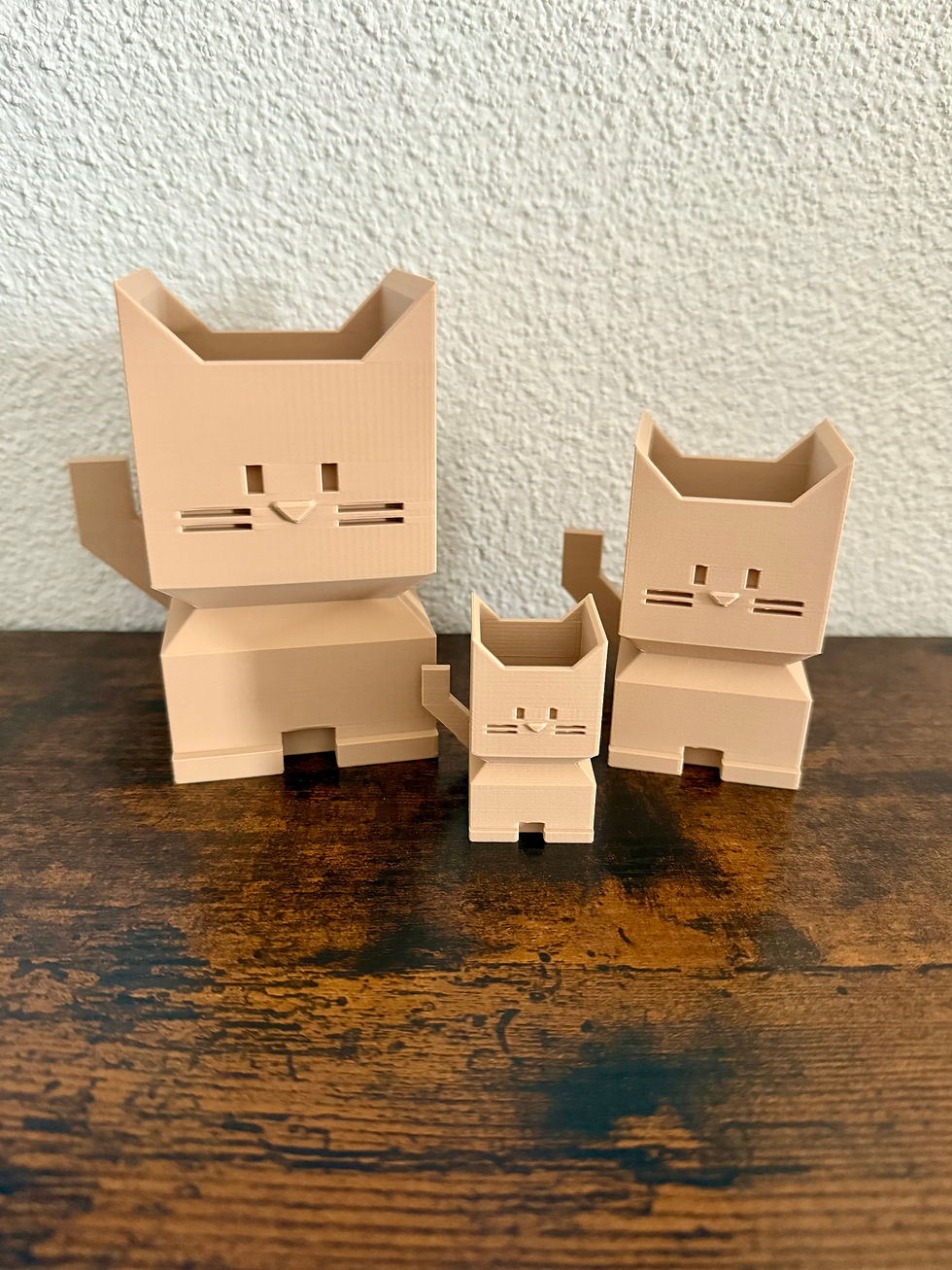 Miniaturbild: Drei beige Katzen-Blumentöpfe stehen nebeneinander auf einer Holzoberfläche. Hinand.