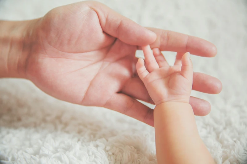 An adult hand holding a baby's hand