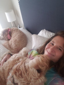Sioux City pet sitter laying in bed with a dog licking her face and another dog laying near her head.
