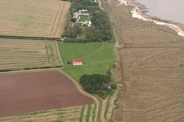 St Peter-on-the-Wall from above, with fields all around, a few trees, and the sea coming into shot in the top corner.