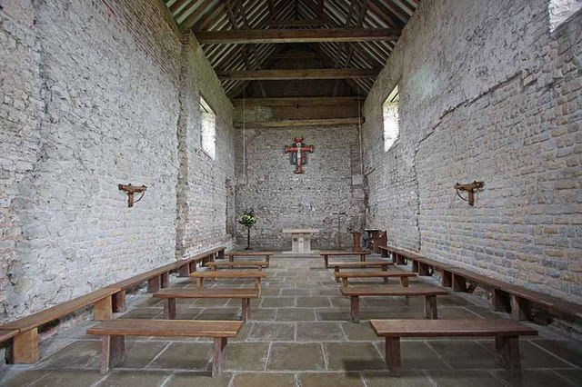 St Peter-on-the-Wall's interior - as plain and functional as the outside. White walls, wooden benches, and a wooden cross on the far wall.