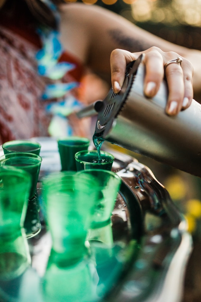 A woman with a flower lei pouring shots out of a tumbler shaker.
