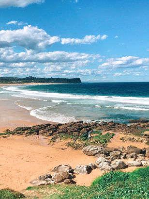 Panoramic view of Warriewood Beach from the south-end rocks, capturing the expansive shoreline and coastal cliffs.
