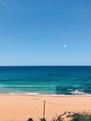 Aerial view of Warriewood Beach from the top carpark, showcasing the sandy shores, rolling waves, and the vastness of the ocean.