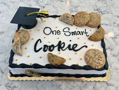A graduation cake with chocolate chip cookies, a grad cap, and broken cookie pieces that reads "one smart cookie"