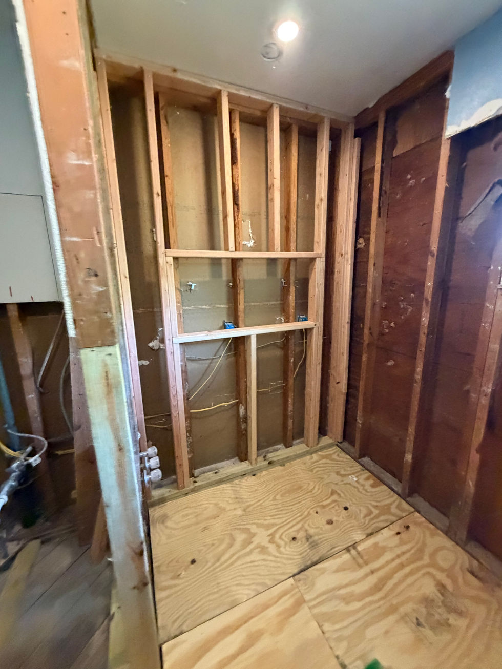 Exposed wood wall framing above newly installed plywood flooring.