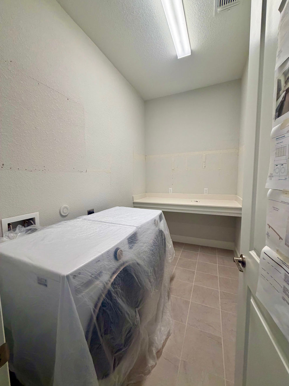 Laundry appliances covered with protective plastic beneath an open wall shelf.