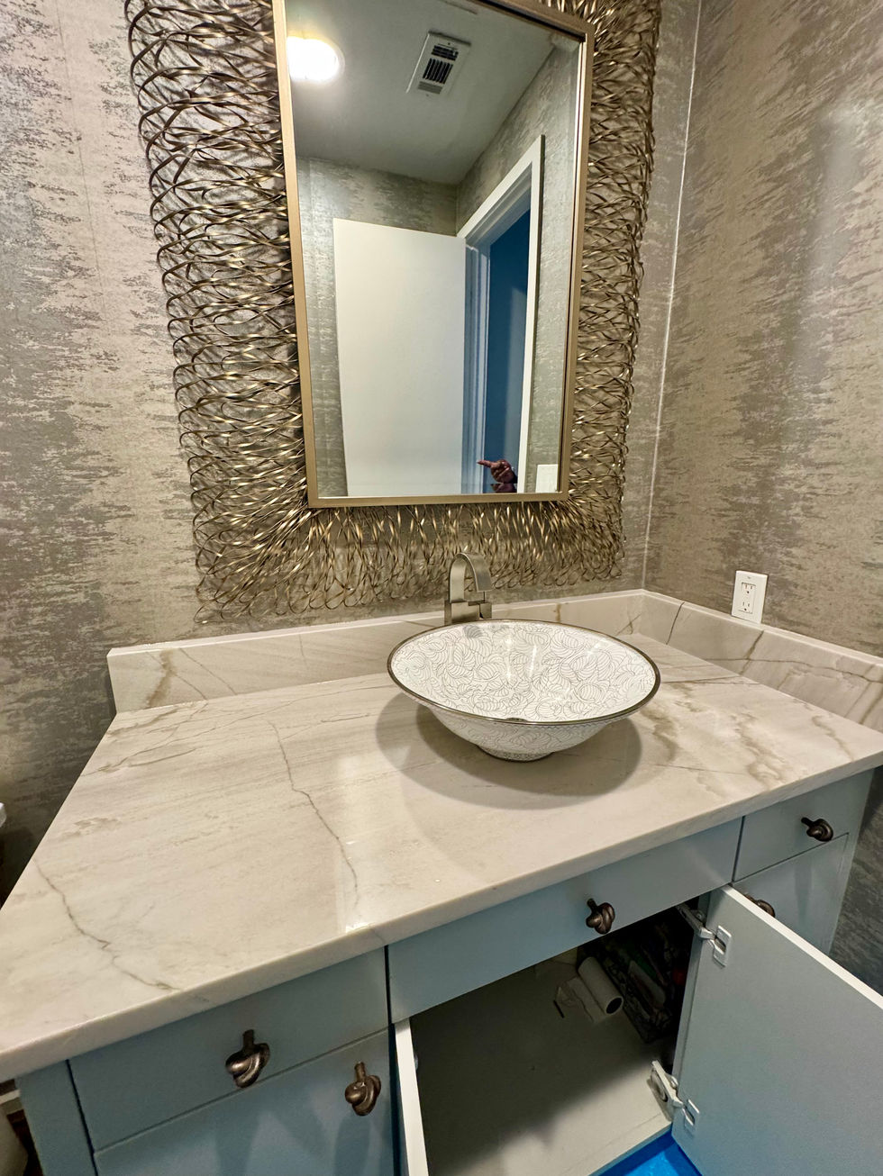 Light granite vanity countertop with a round vessel sink beneath a framed mirror.