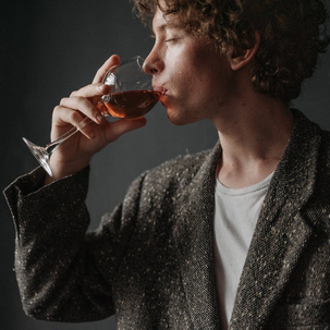 A young man drinking red wine that will stain teeth needing teeth whitening