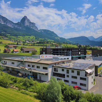 Modernes Gebäude mit Solaranlagen vor beeindruckender Alpenlandschaft.