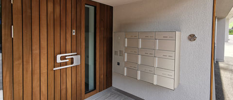 Moderne Holztür mit Glaspaneel und Briefkästen im Eingangsbereich.