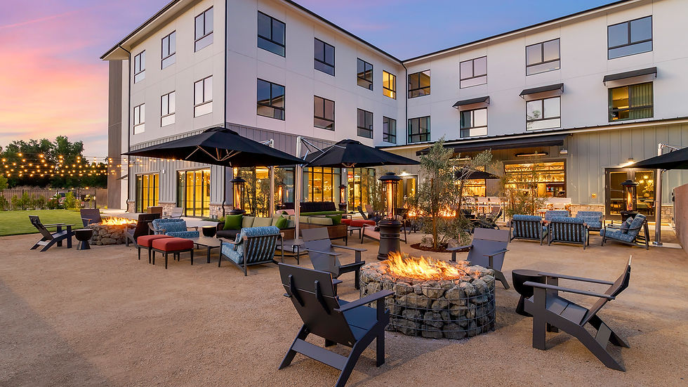 Cambria Hotel courtyard at sunset with fire pits, lounge chairs, black umbrellas, string lights, and warm glowing windows