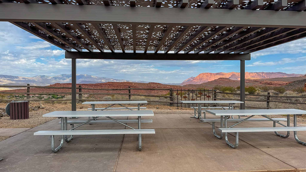 Picnic area with metal tables under a patterned canopy. Desert landscape and mountains in the background. Clear skies, tranquil setting.